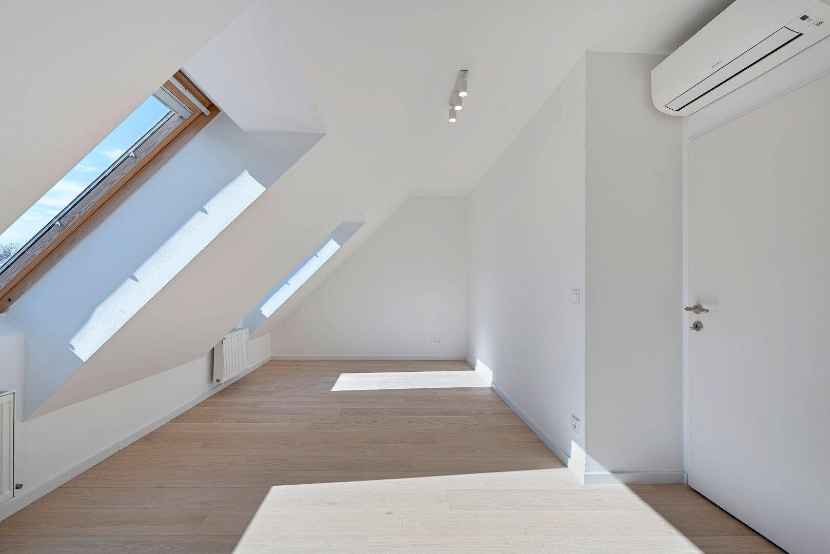 Lichtdurchfluteter Dachgeschossraum mit Holzboden, schrägen Wänden und Dachfenstern, ideal als Wohnbereich.