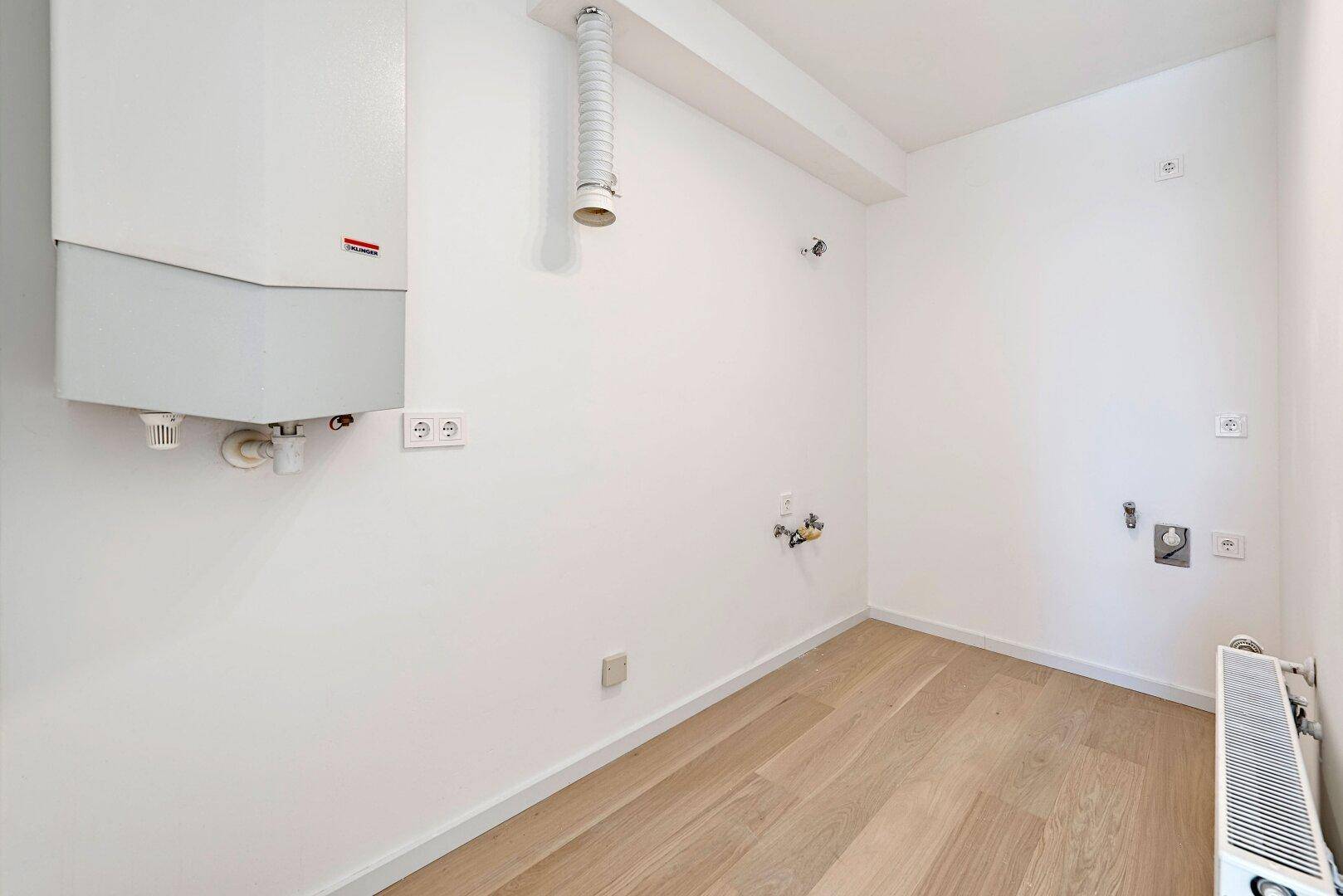 Hauswirtschaftsraum mit Heizungsanlage, Anschlüssen für Waschmaschine und Holzboden.