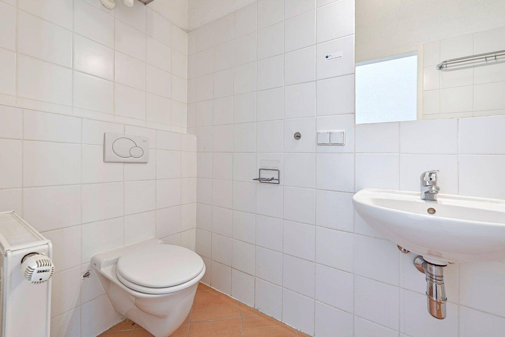Kleines WC mit Wand-WC, Waschbecken und weißen Fliesen.