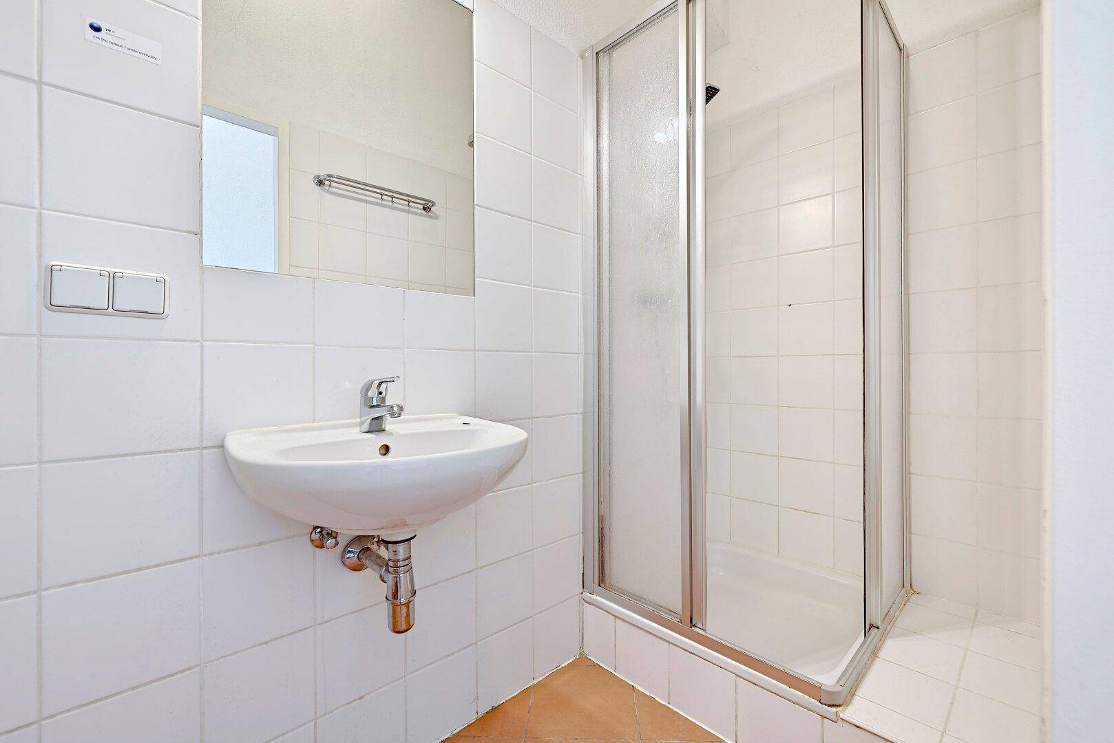 Badezimmer mit Duschkabine, Waschbecken und weißen Wandfliesen.