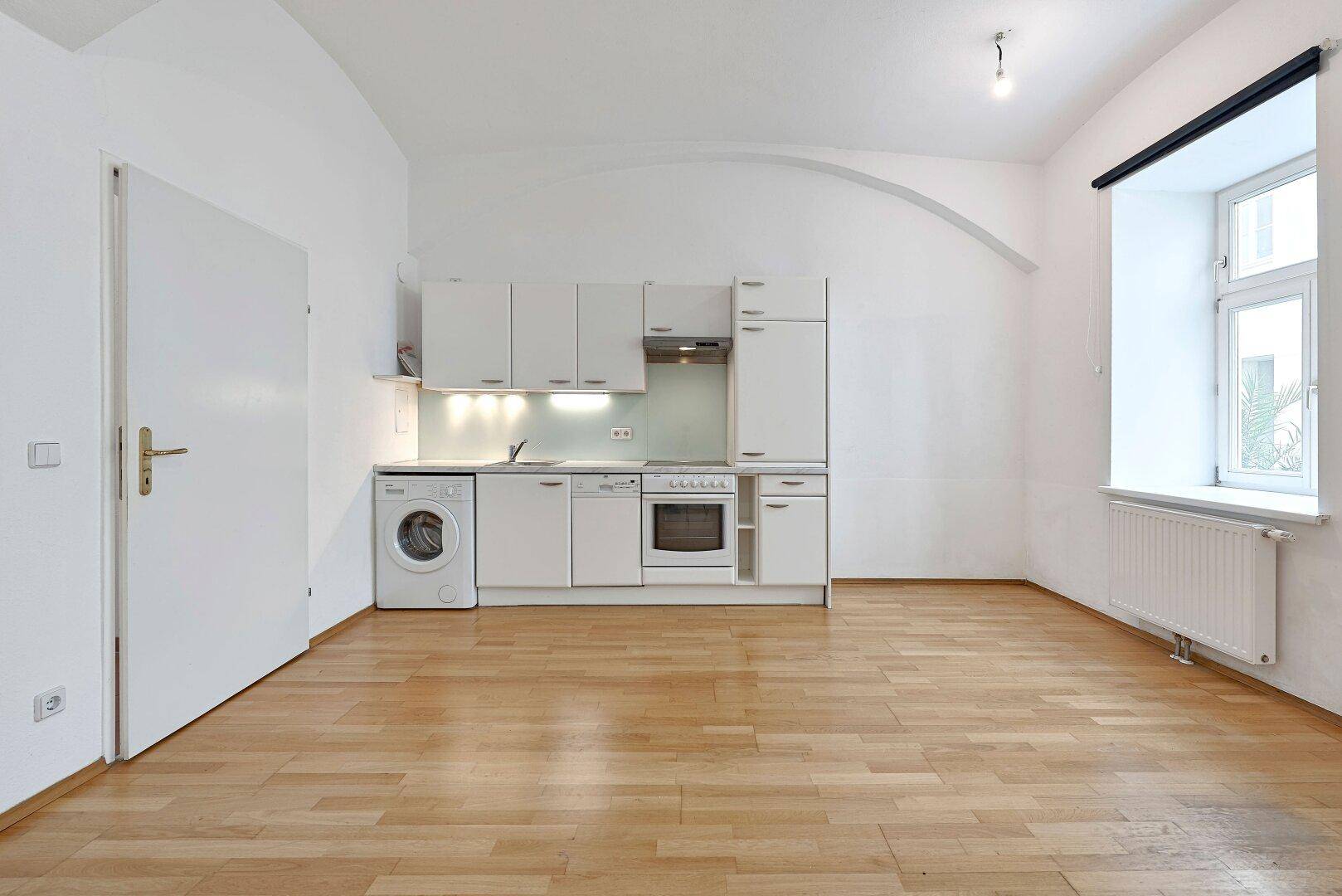 Funktionale Küchenzeile mit Fenster und Heizkörper in einem hellen Raum mit Holzboden.