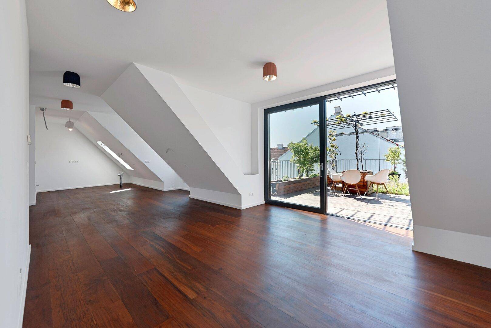 Geräumiger Wohnbereich mit dunklem Parkettboden, Dachschrägen und direktem Zugang zur Dachterrasse.