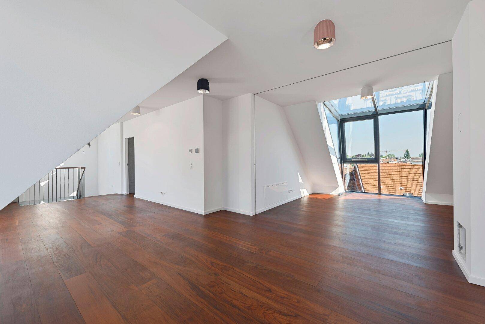 Heller, offener Wohnbereich mit dunklem Holzfußboden, Dachschrägen und großen Glasfenstern.