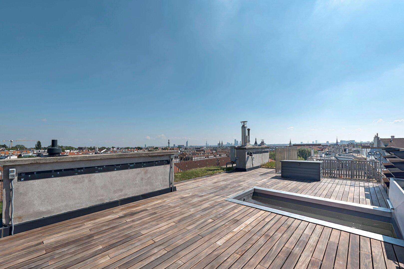 Moderne Dachterrasse mit Holzdeck, integriertem Wasserbecken und weitem Stadtblick.