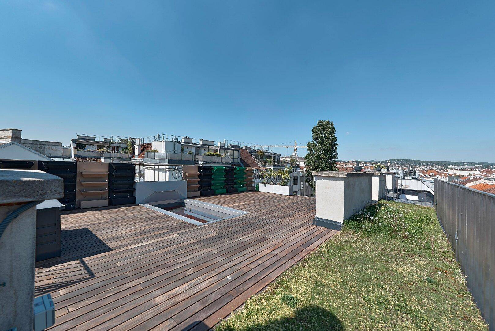 Weitläufige Dachterrasse mit Holzdeck und begrünten Flächen, umgeben von Stadtgebäuden.