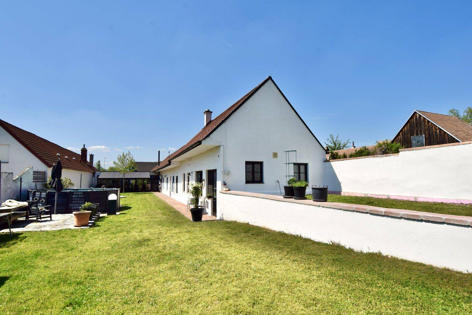 Seitenansicht des Hauses mit weißer Fassade, Rasenfläche und einer niedrigen Mauer.