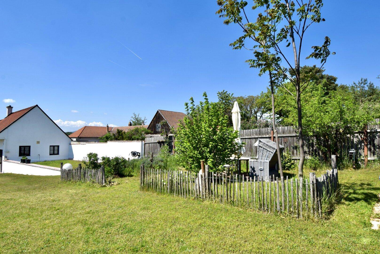 Großer Gartenbereich mit Rasen, Bäumen und einem kleinen umzäunten Bereich im Hintergrund.
