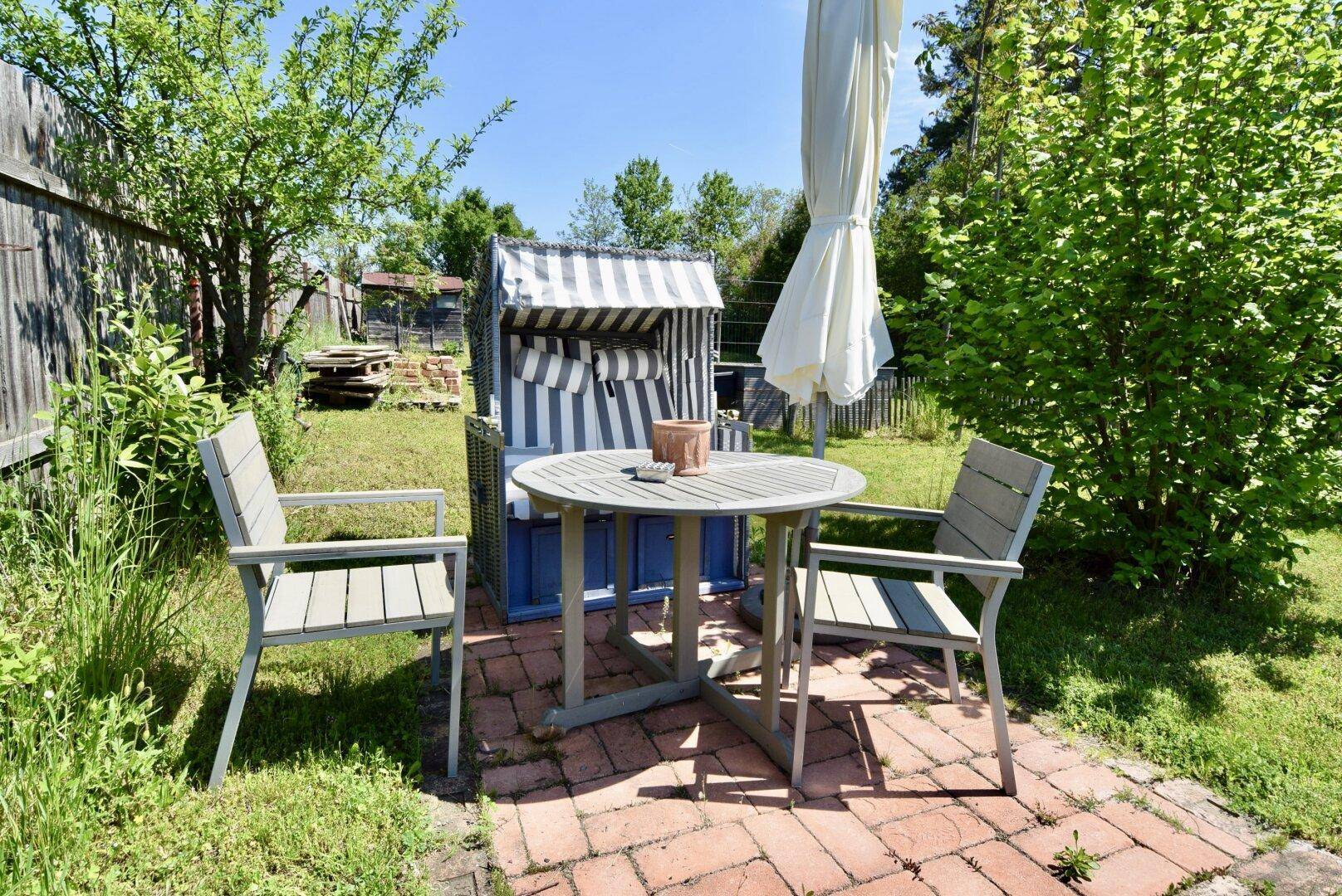 Gemütlicher Sitzbereich im Garten mit Tisch, Stühlen und Strandkorb, umgeben von Grün.