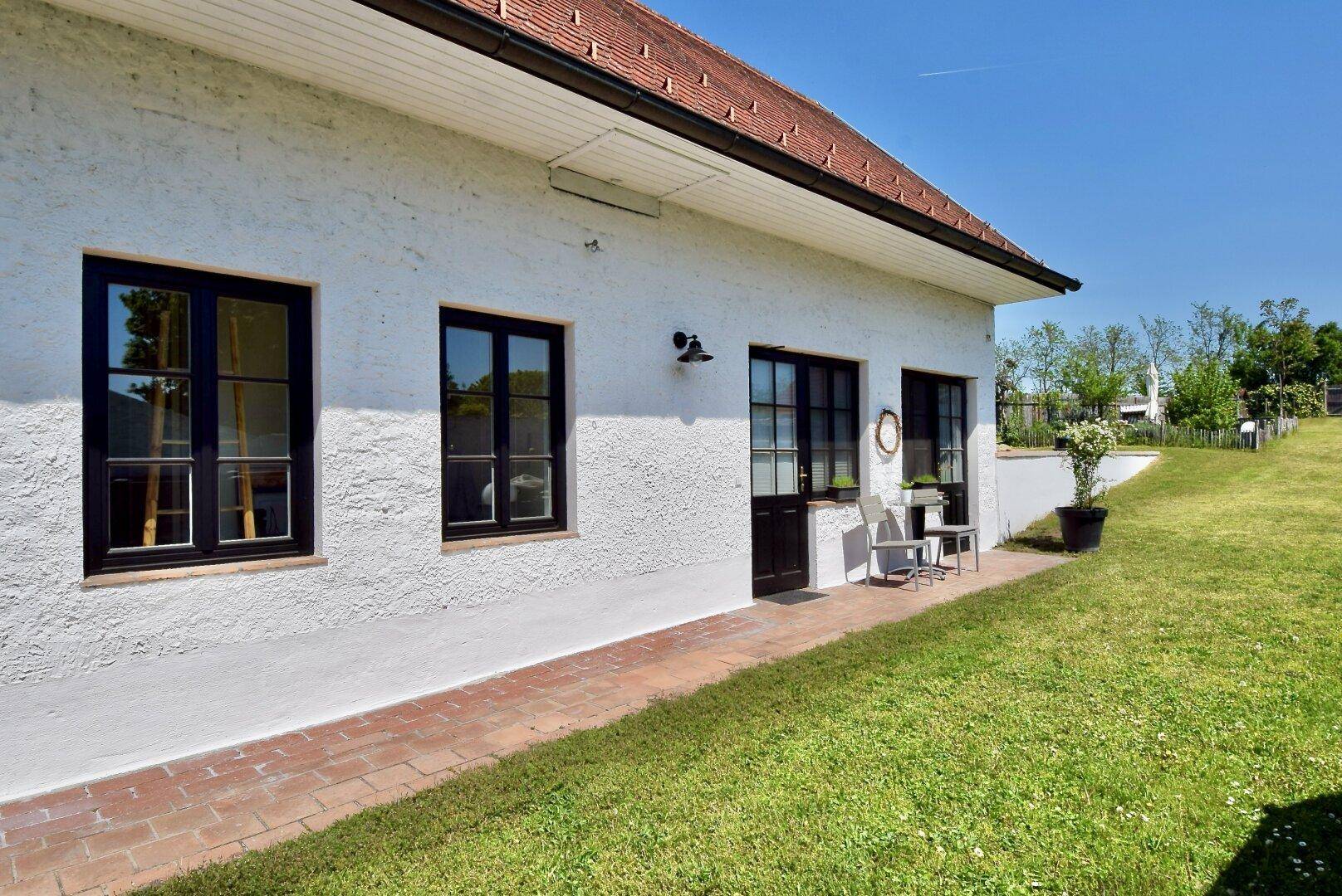Seitenansicht des Hauses mit weißer Fassade, schwarzen Fenstern und einem gepflasterten Weg.