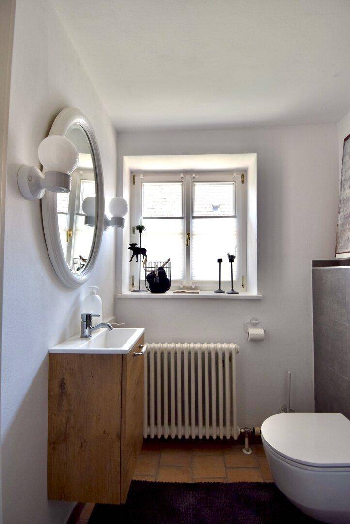 Kleines Gäste-WC mit Fenster, wandmontiertem Waschbecken und Heizkörper, funktional und hell.