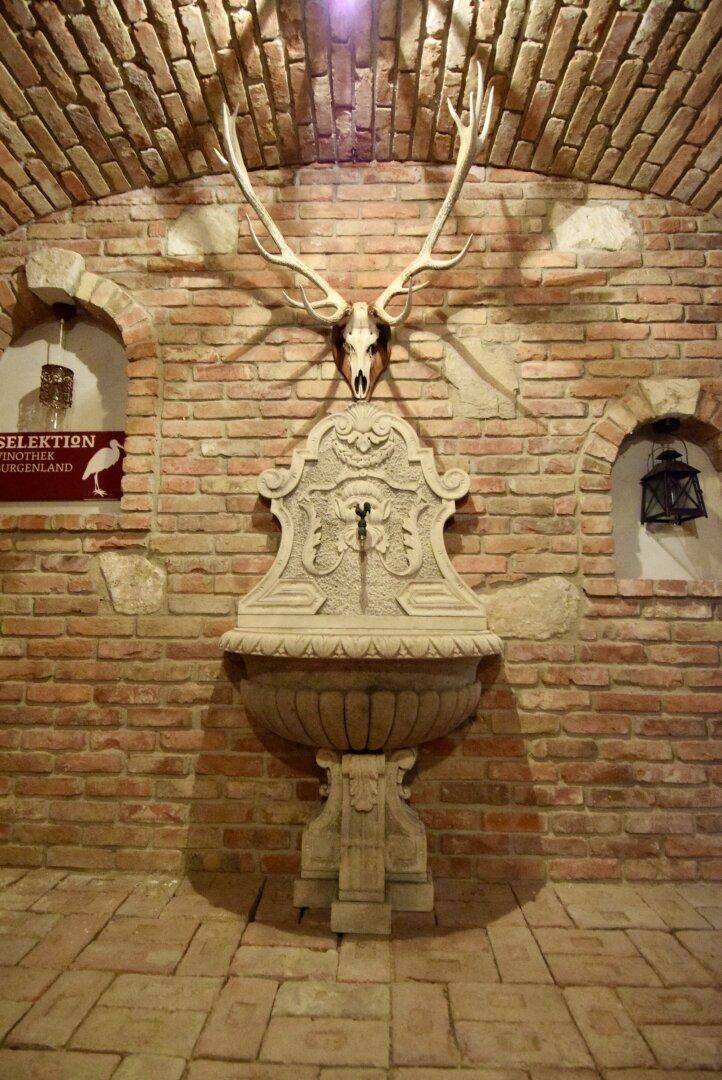 Detailansicht eines kunstvollen Steinbrunnens mit Hirschgeweih in einem rustikalen Ziegelkeller.
