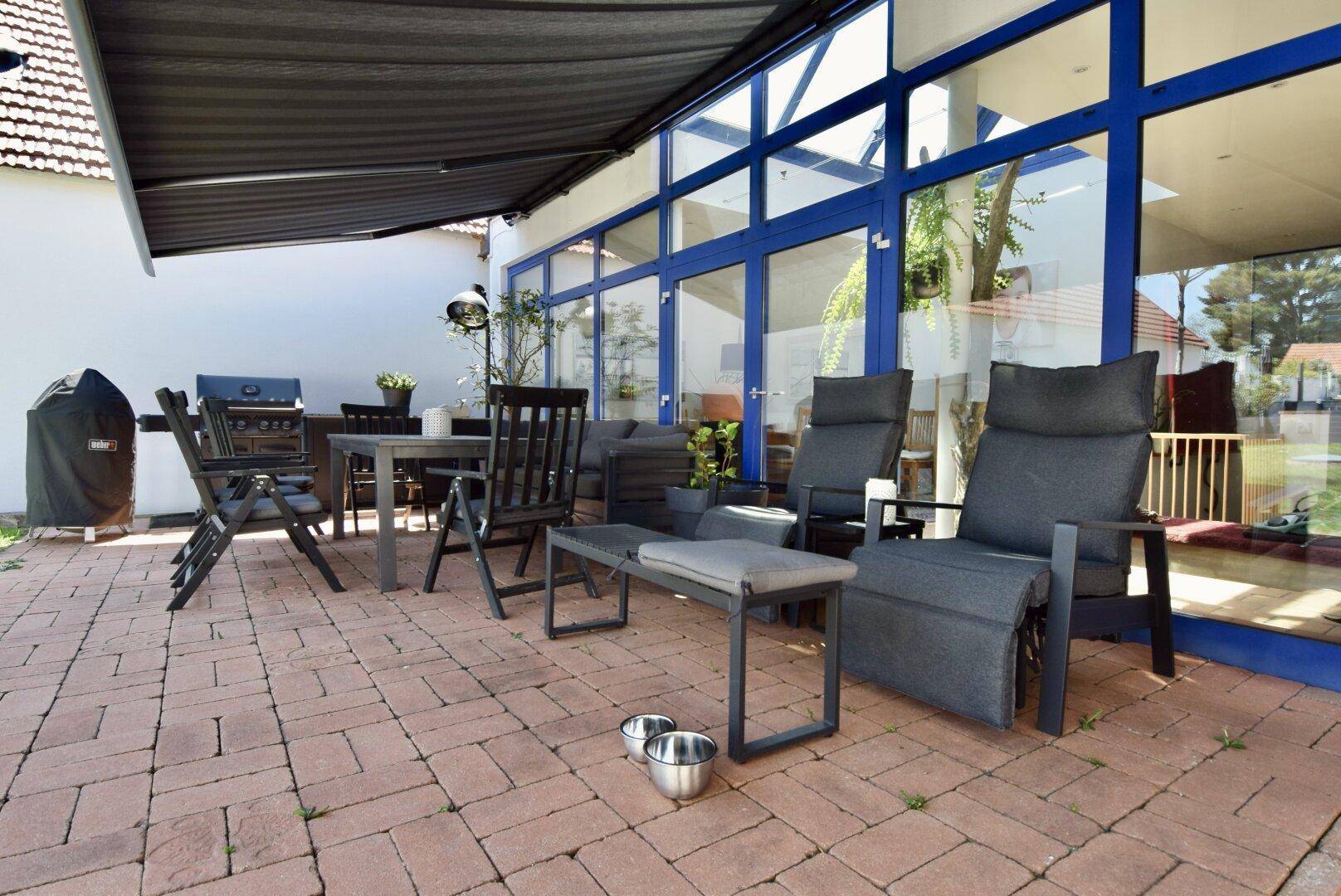 Gemütliche Terrasse mit bequemen Lounge-Sesseln, Esstisch und einem ausfahrbaren Sonnenschutz.