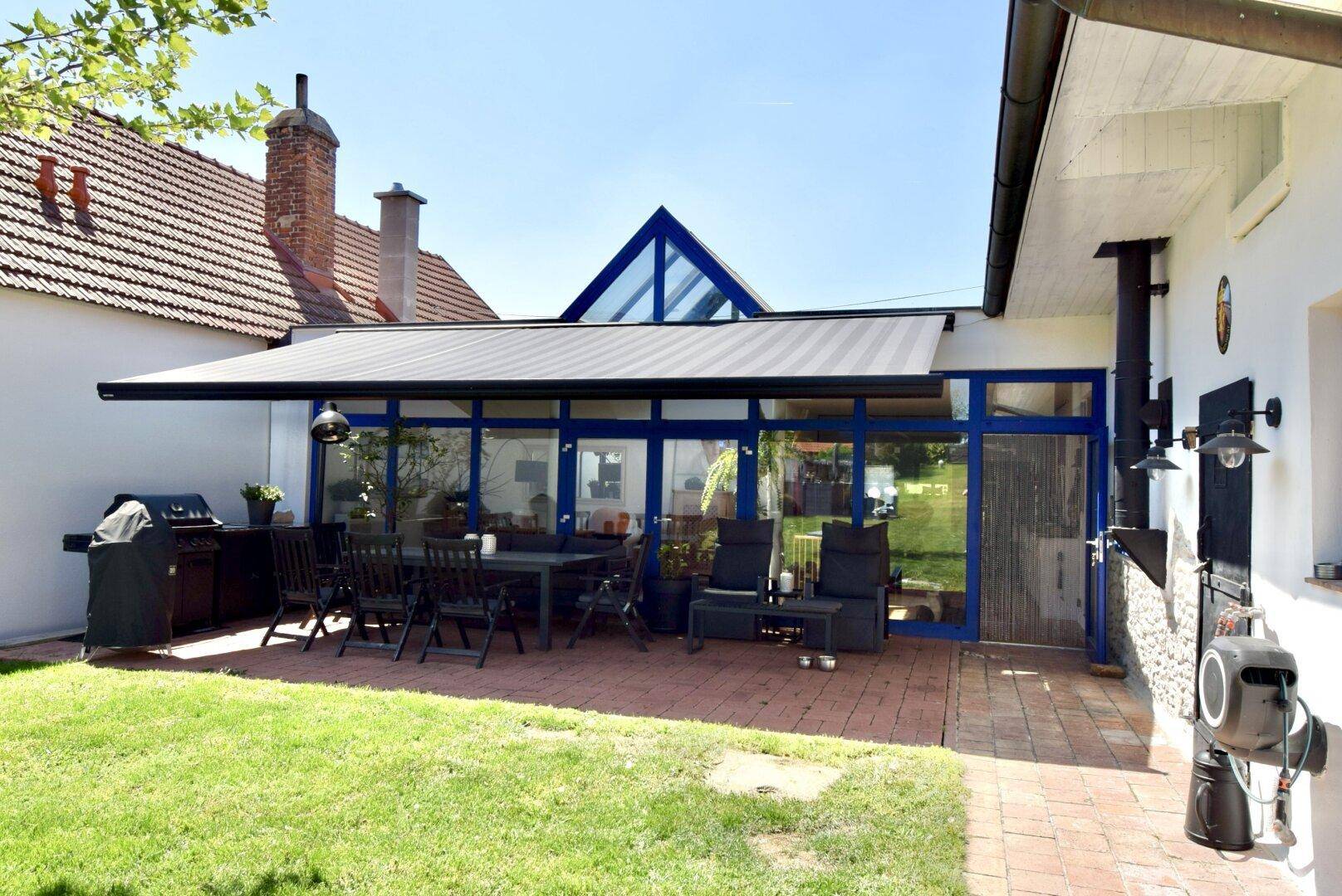 Große gepflasterte Terrasse mit Esstisch, Lounge-Möbeln und einem modernen Wintergarten.