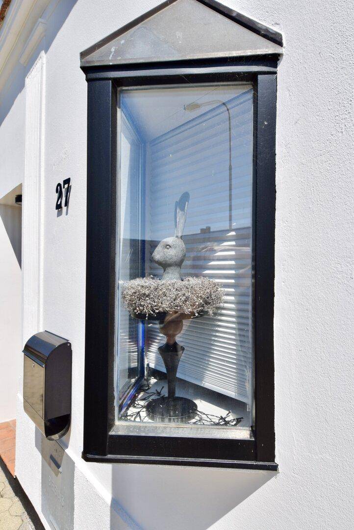 Detailansicht eines Erkerfensters mit Hasenfigur und Hausnummer 27 an der weißen Fassade.
