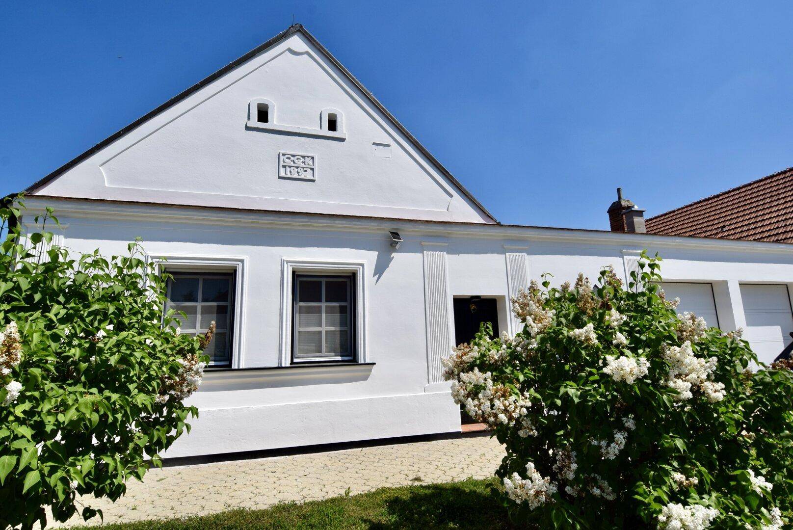 Historische weiße Hausfassade mit Giebeldach und blühenden Sträuchern im Vorgarten.