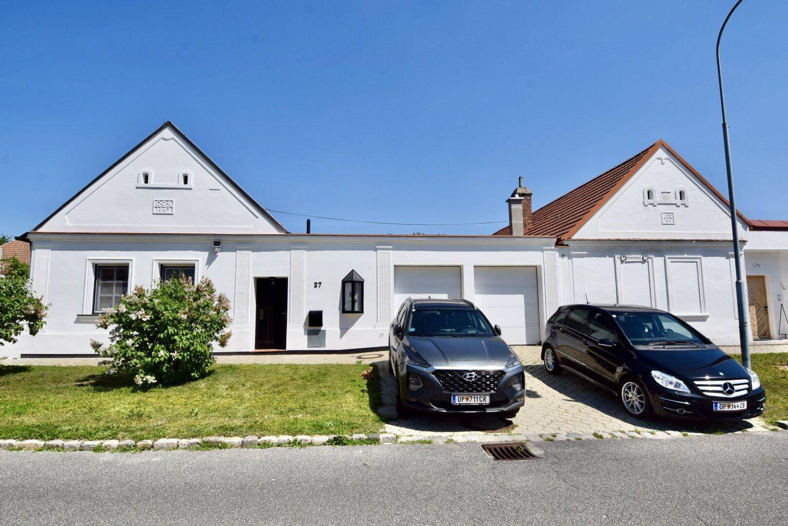 Vorderansicht des Hauses von der Straße mit zwei geparkten Autos und Garagentoren.