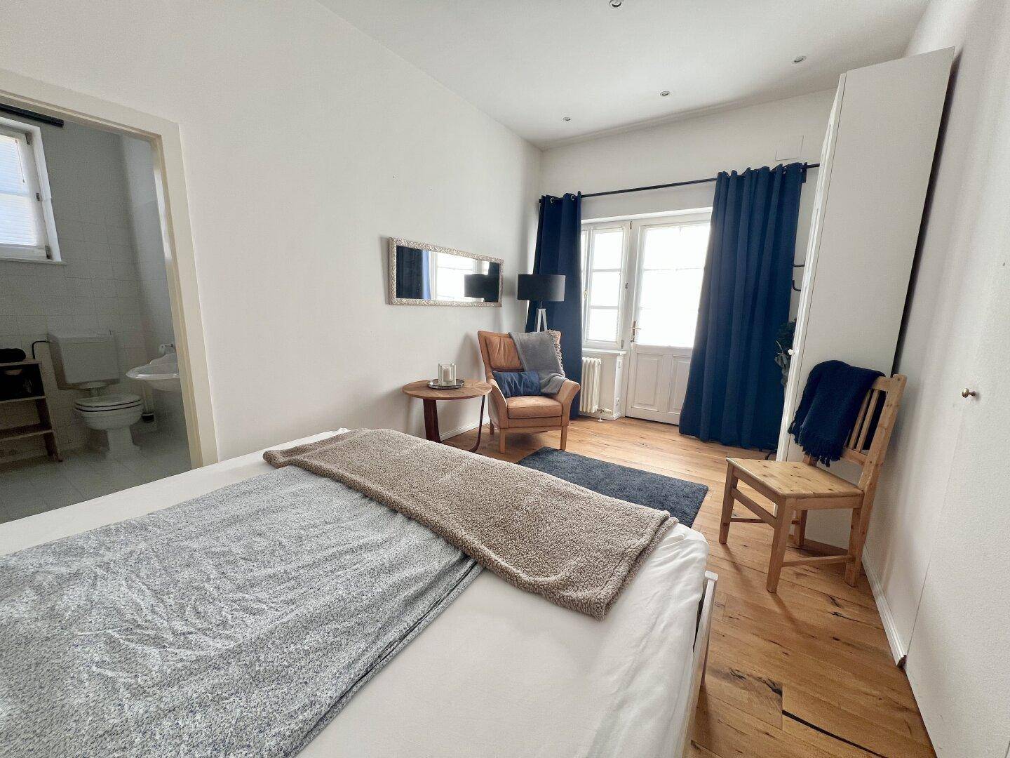 Helles Schlafzimmer mit Holzboden, Zugang zu einem Balkon und einem angrenzenden Badezimmer.