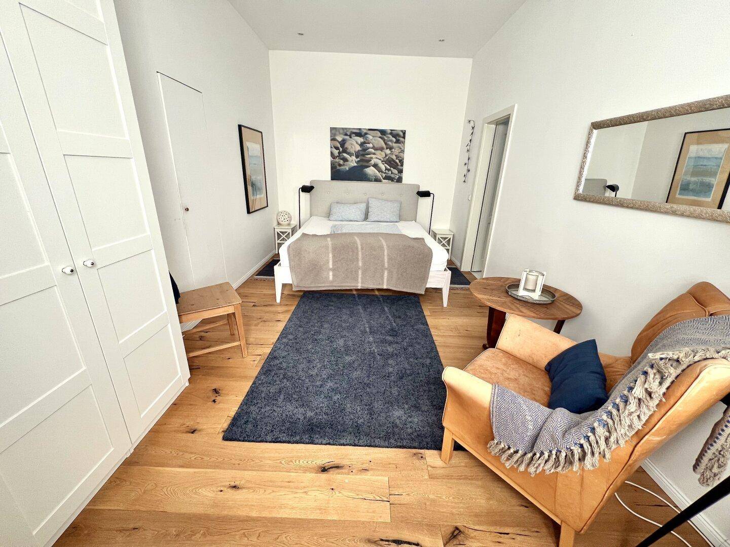 Geräumiges Schlafzimmer mit Holzboden, großem Bett und bequemen Ledersessel, einladend und hell.