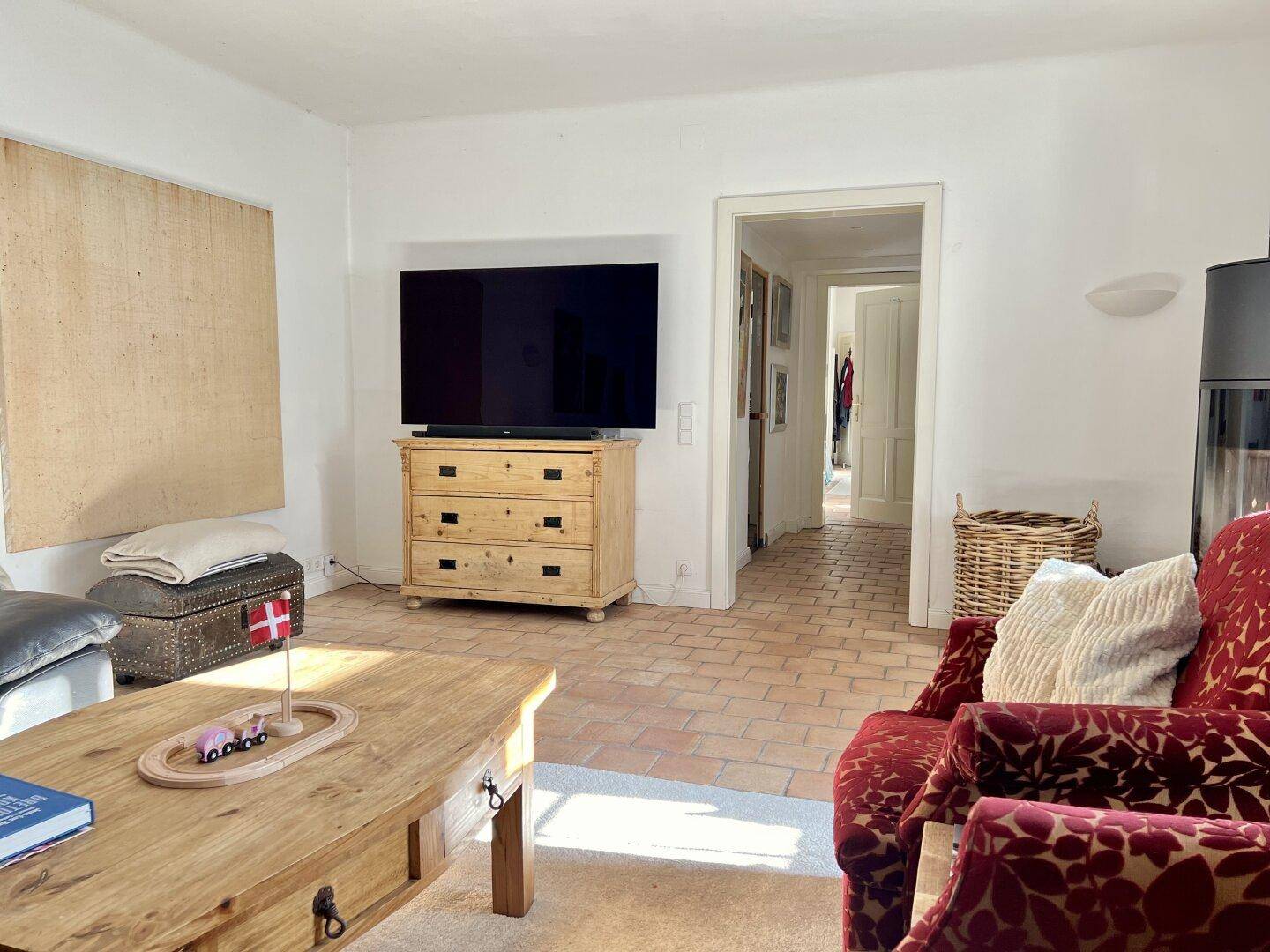 Helles Wohnzimmer mit Terrakottafliesen, Holztisch und Kaminofen, der eine gemütliche Atmosphäre schafft.