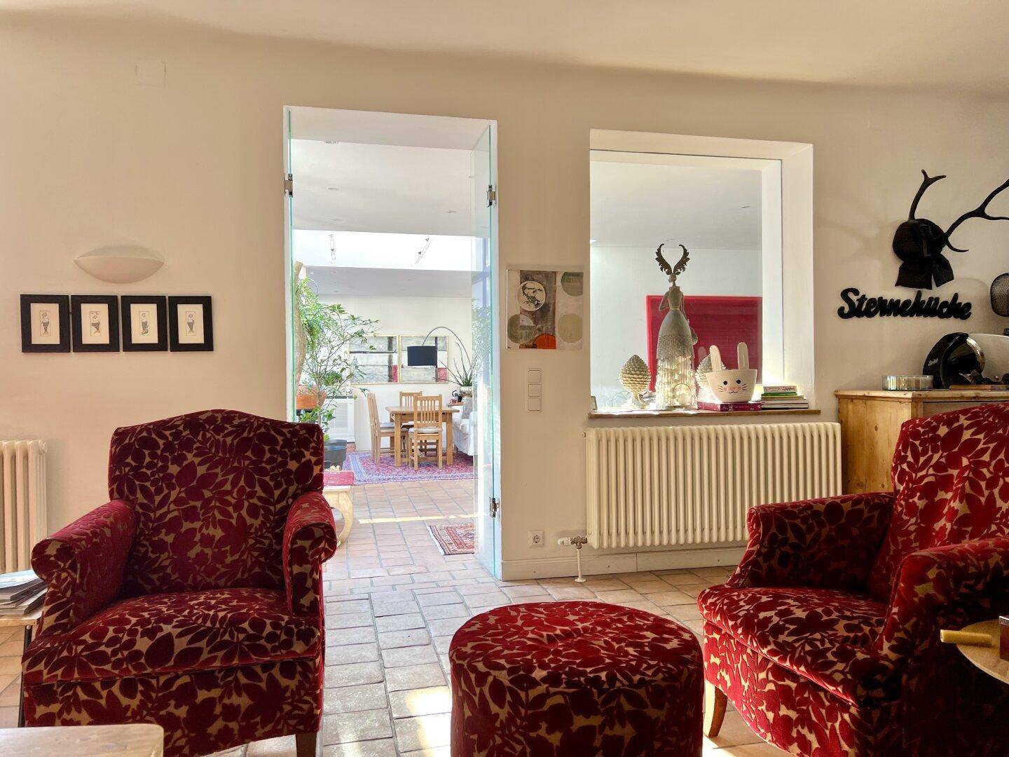 Helles Wohnzimmer mit Terrakottaboden, roten Sesseln und Blick in den angrenzenden Wintergarten.