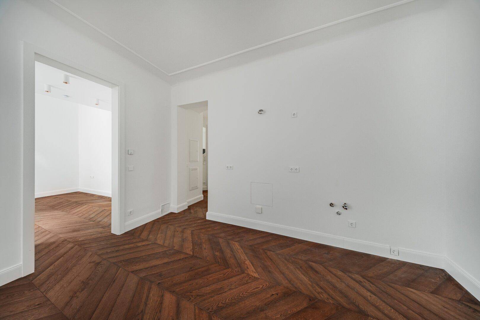 Geräumiges Zimmer mit Fischgrätparkett und mehreren Türöffnungen, bietet flexible Gestaltungsmöglichkeiten.