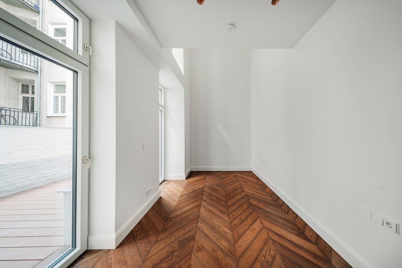 Langer, heller Flur mit Fischgrätparkett und großem Fenster, das viel Tageslicht hereinlässt.