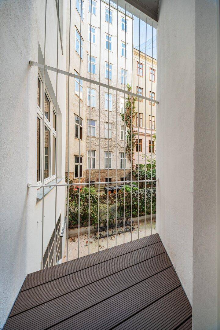 Französischer Balkon mit Blick auf den begrünten Innenhof und die umliegenden Gebäude.