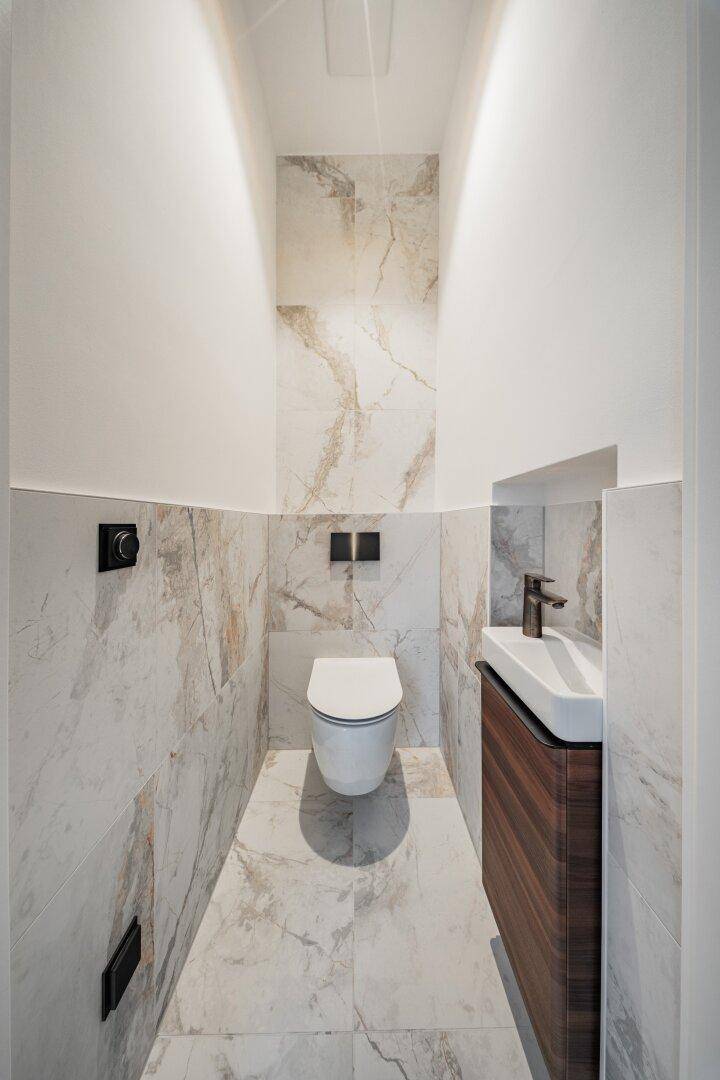 Modernes Gäste-WC mit eleganten Marmorfliesen, wandhängendem WC und kleinem Waschtisch.