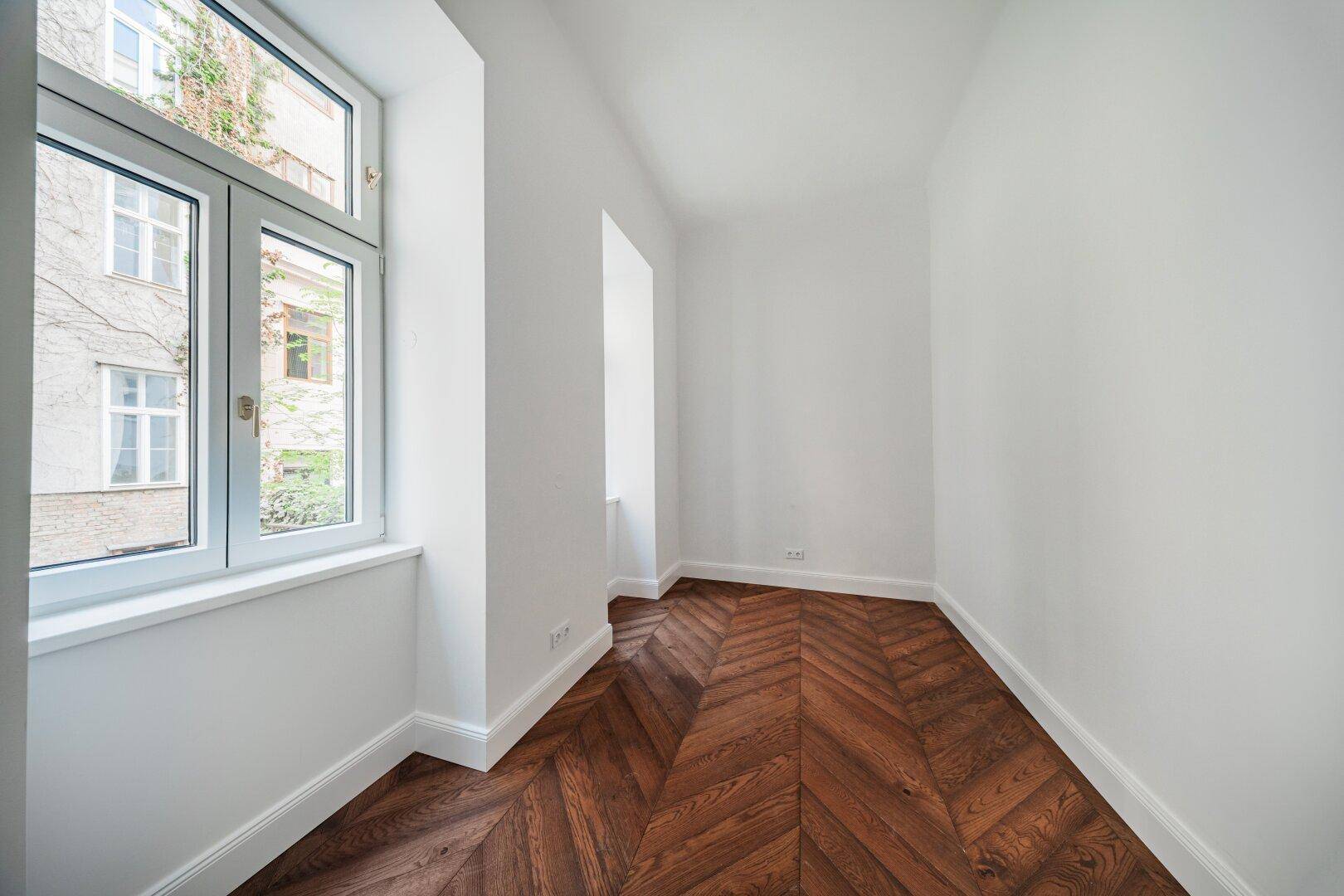 Kleiner, heller Raum mit Fischgrätparkett und zwei Fenstern, ideal als Arbeitszimmer.
