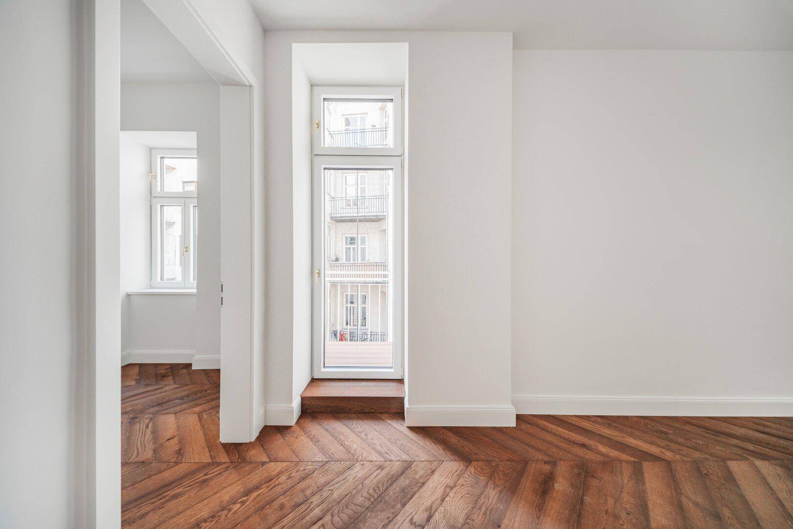 Helles Zimmer mit Fischgrätparkett und einem französischen Balkon mit Blick auf die Straße.