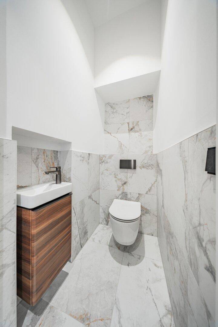 Elegantes Gäste-WC mit Wand-WC, kleinem Waschbecken und Marmorfliesen.