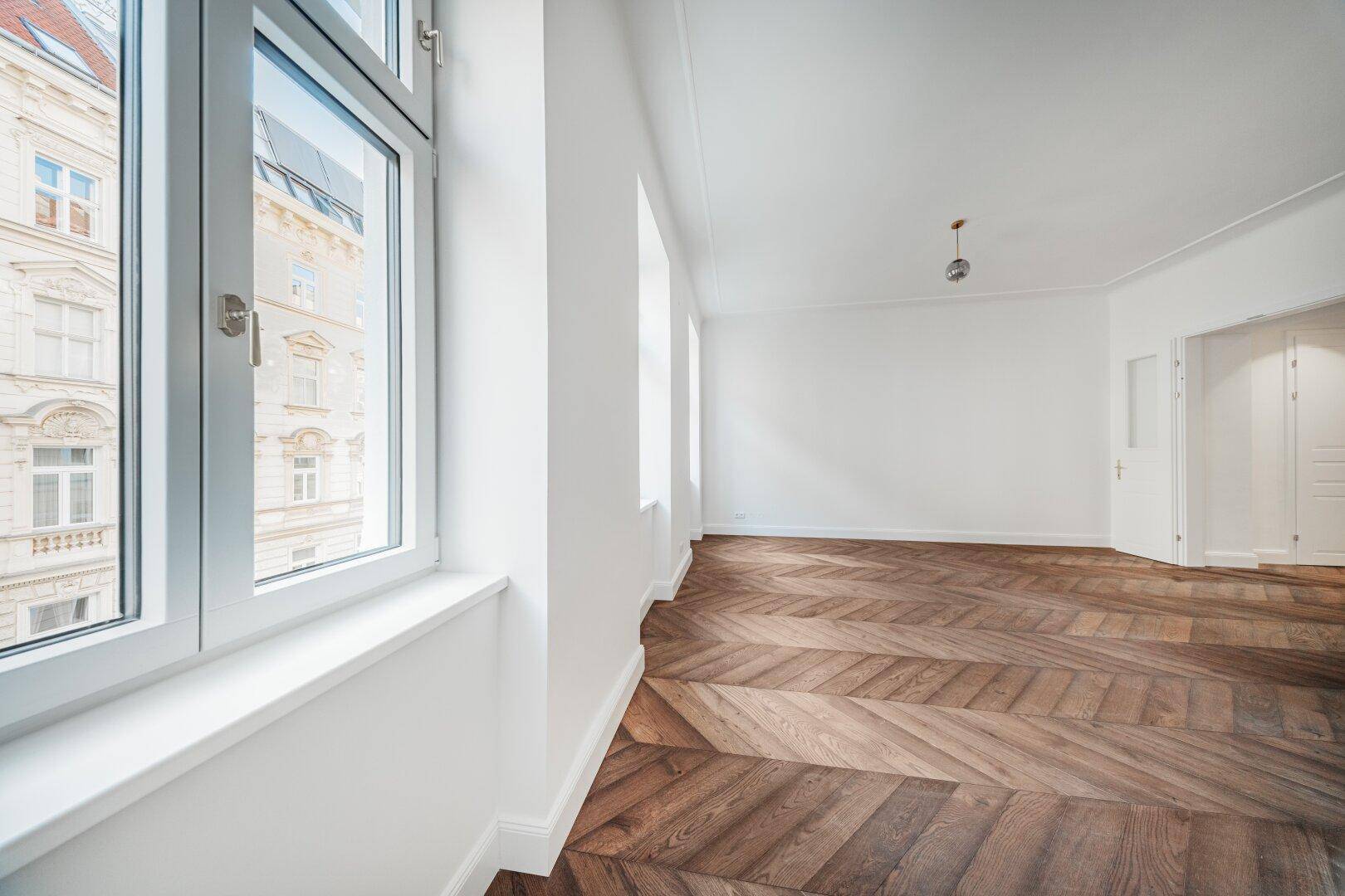 Detailansicht eines großen Fensters in einem hellen Raum mit Fischgrätparkett.