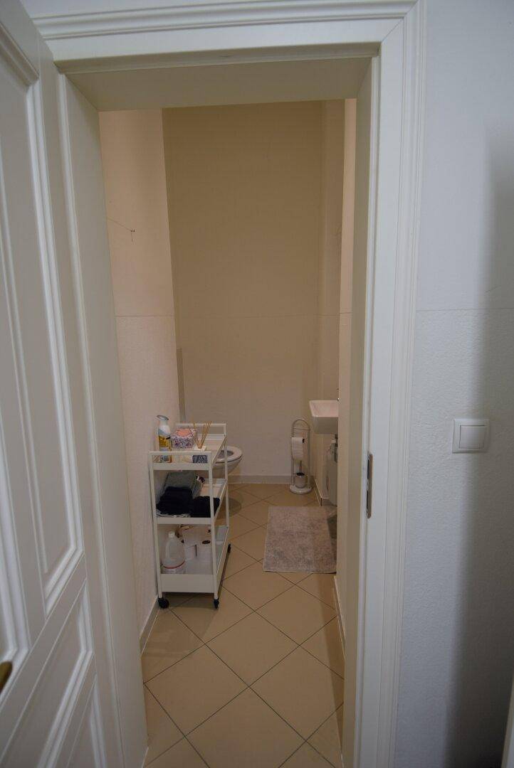 Kleiner Toilettenraum mit beigefarbenen Fliesen, Waschbecken und WC, durch eine offene Tür sichtbar.
