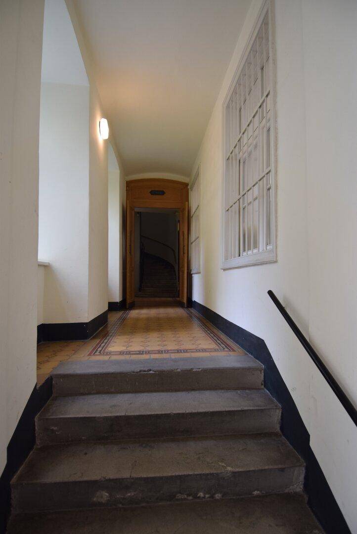 Treppenhaus in einem Flur mit gemustertem Fliesenboden, gewölbter Decke und Fenstern mit Gitterstäben.