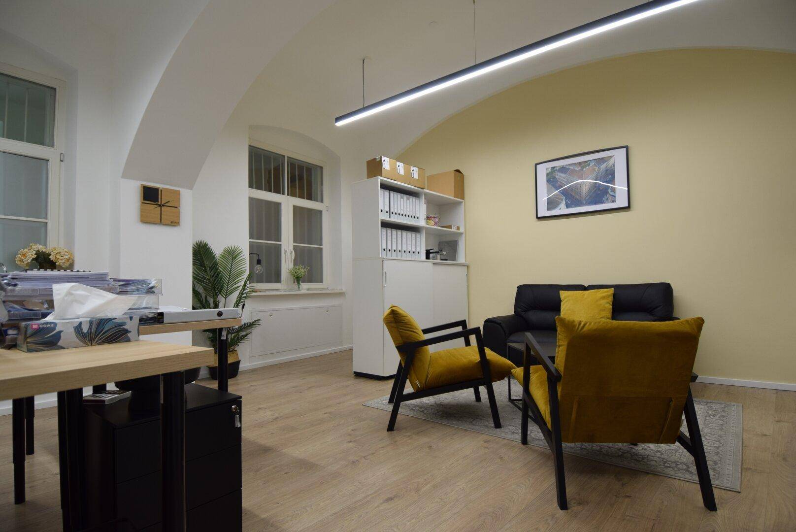 Helles Büro mit gemütlicher Sitzecke, gelber Akzentwand, Holzboden und gewölbter Decke, ideal für Besprechungen.