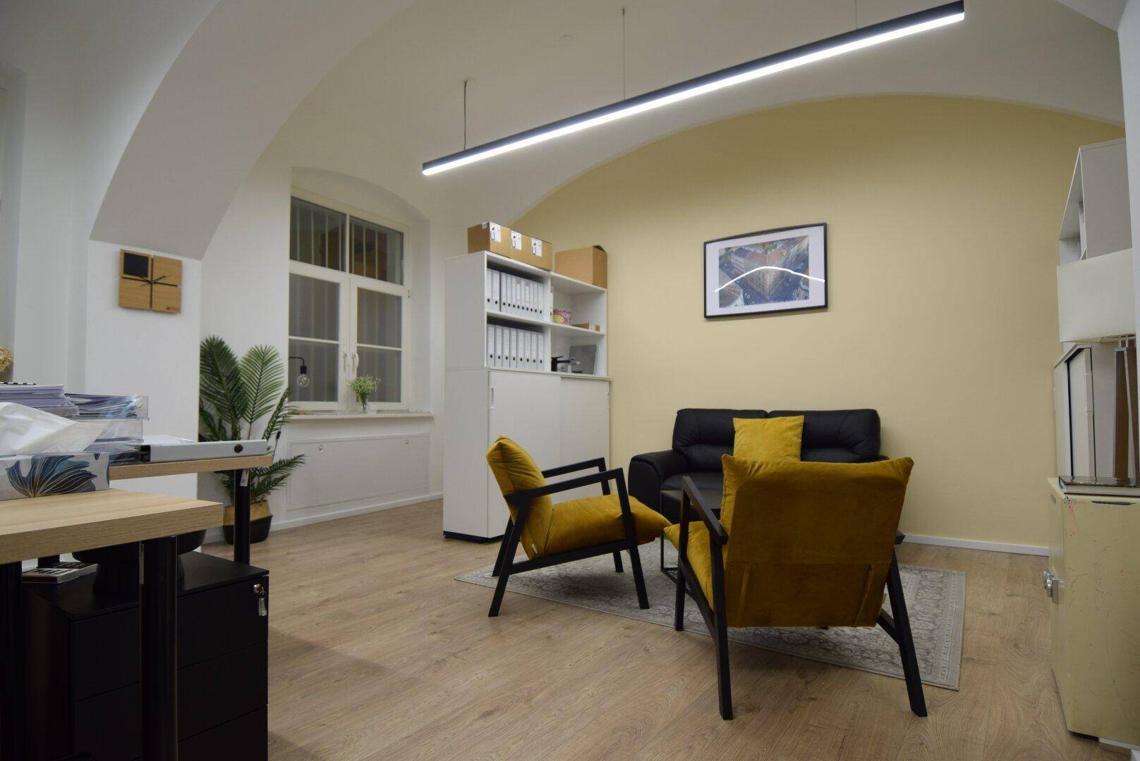 Helles Büro mit gemütlicher Sitzecke, gelber Akzentwand, Holzboden und gewölbter Decke, ideal für Besprechungen.