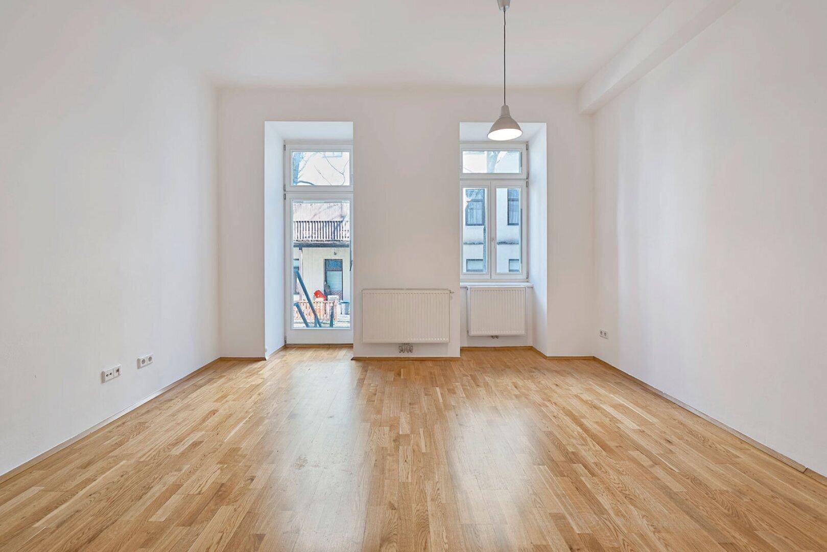 Helles Zimmer mit Parkettboden und zwei großen Fenstern, bereit zur individuellen Einrichtung.