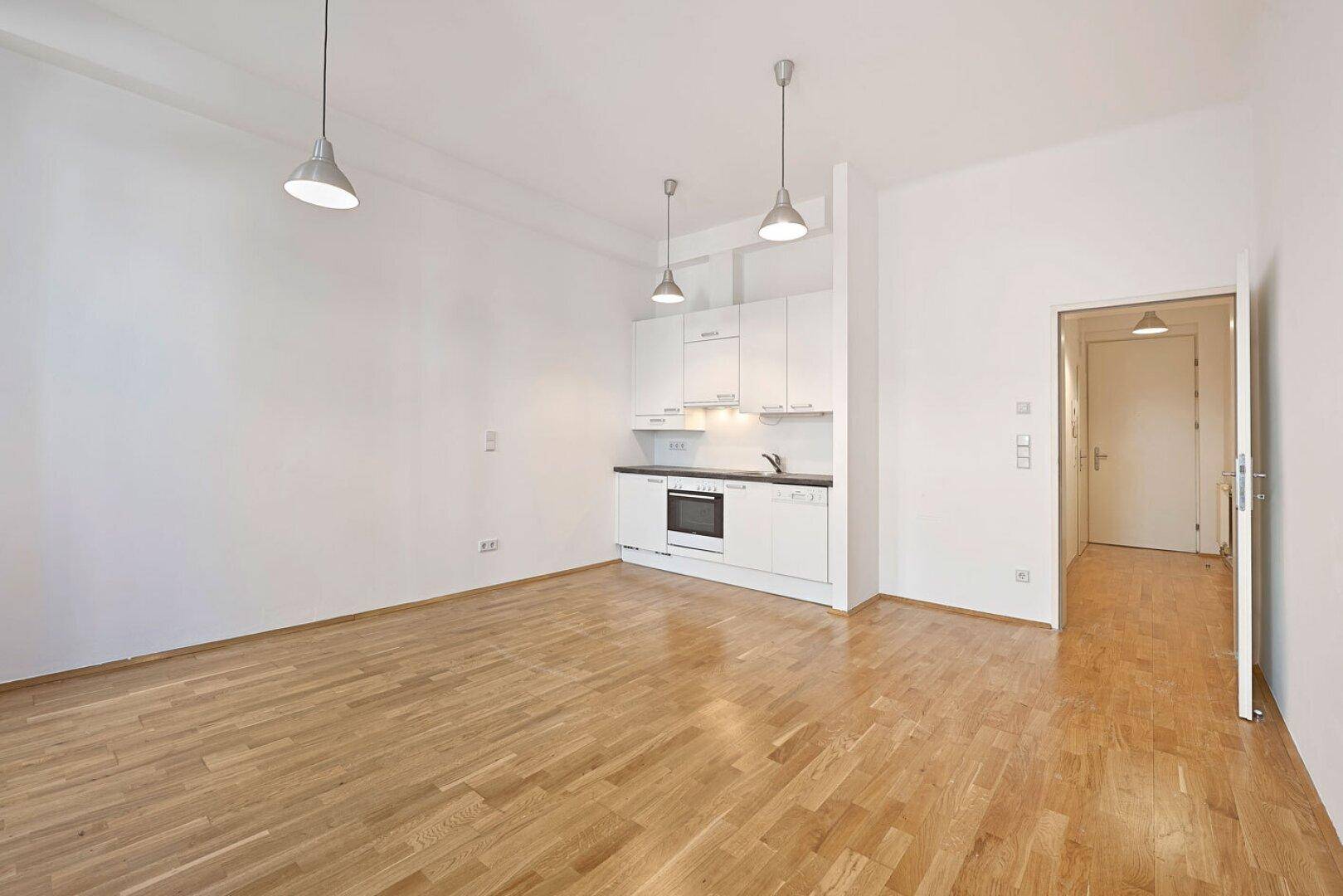 Heller Wohnbereich mit integrierter Küchenzeile und Parkettboden, ideal für ein Studio-Apartment.