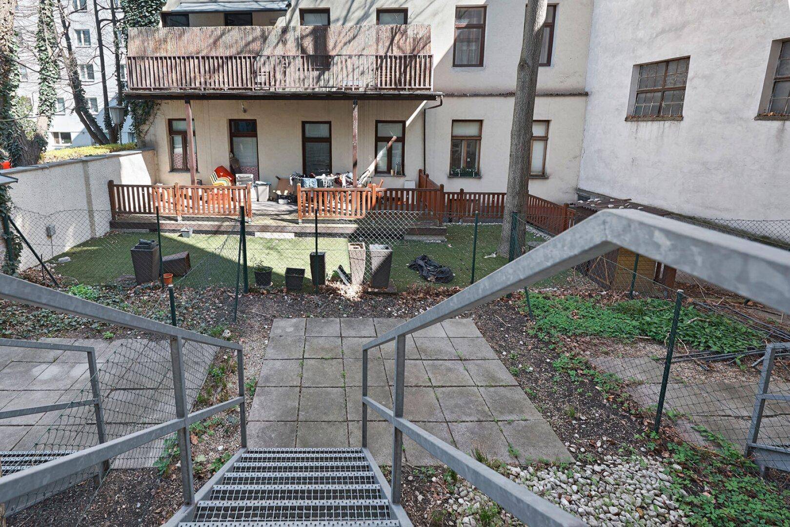 Gartenbereich mit Treppenzugang und einer weiteren Terrasse im Hintergrund des Gebäudes.