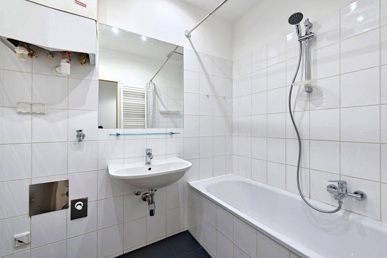Gefliestes Badezimmer mit Badewanne, Waschbecken und Spiegel, in gutem Zustand.