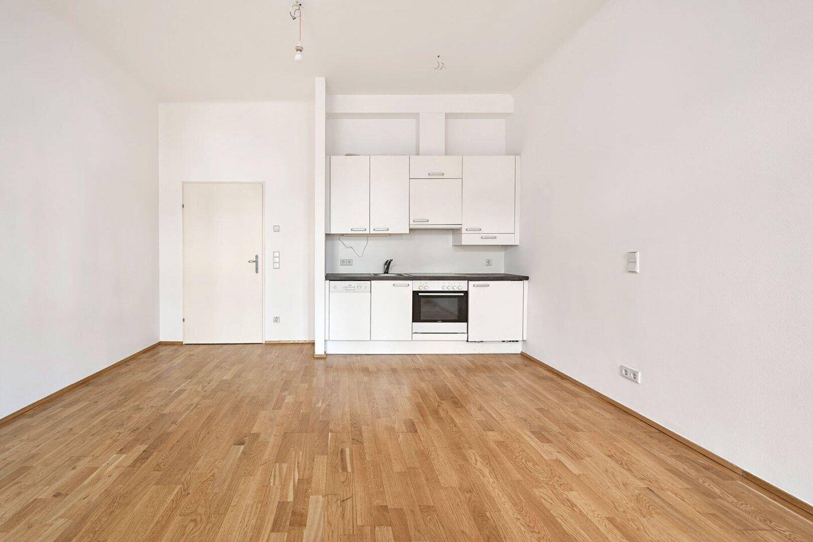 Heller Wohnbereich mit integrierter Küchenzeile, Holzboden und weißen Schränken.