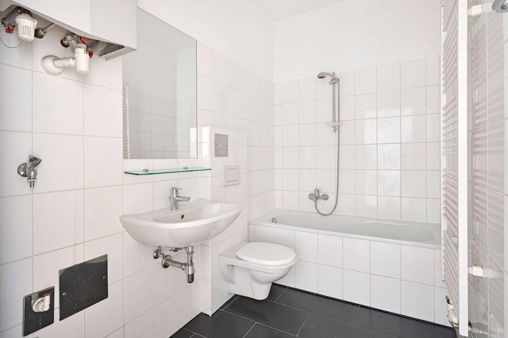 Modernes Badezimmer mit weißen Fliesen, dunklem Boden, Badewanne mit Dusche und Handtuchheizkörper.