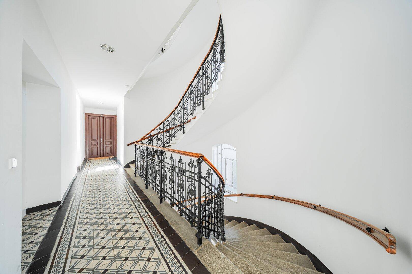 Elegantes Treppenhaus mit schmiedeeisernem Geländer und gemustertem Fliesenboden, führt zu den Etagen.