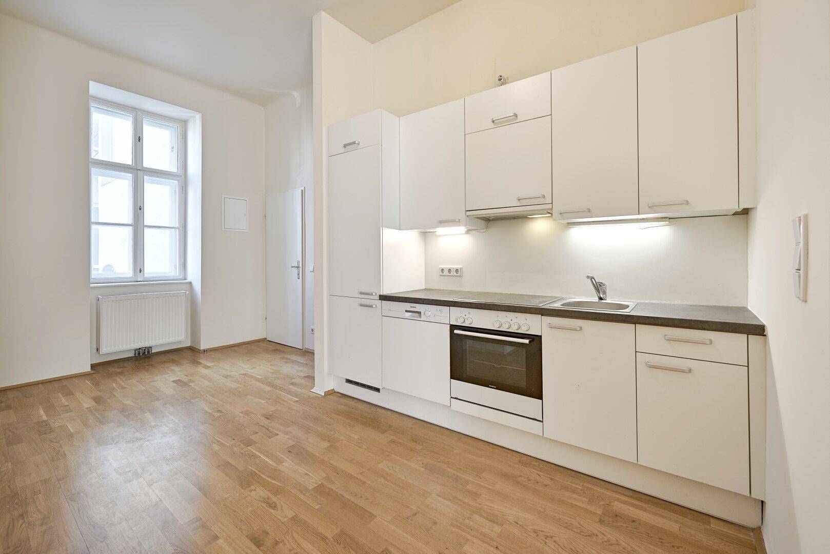 Funktionale Einbauküche mit weißen Schränken, dunkler Arbeitsplatte und integriertem Backofen.