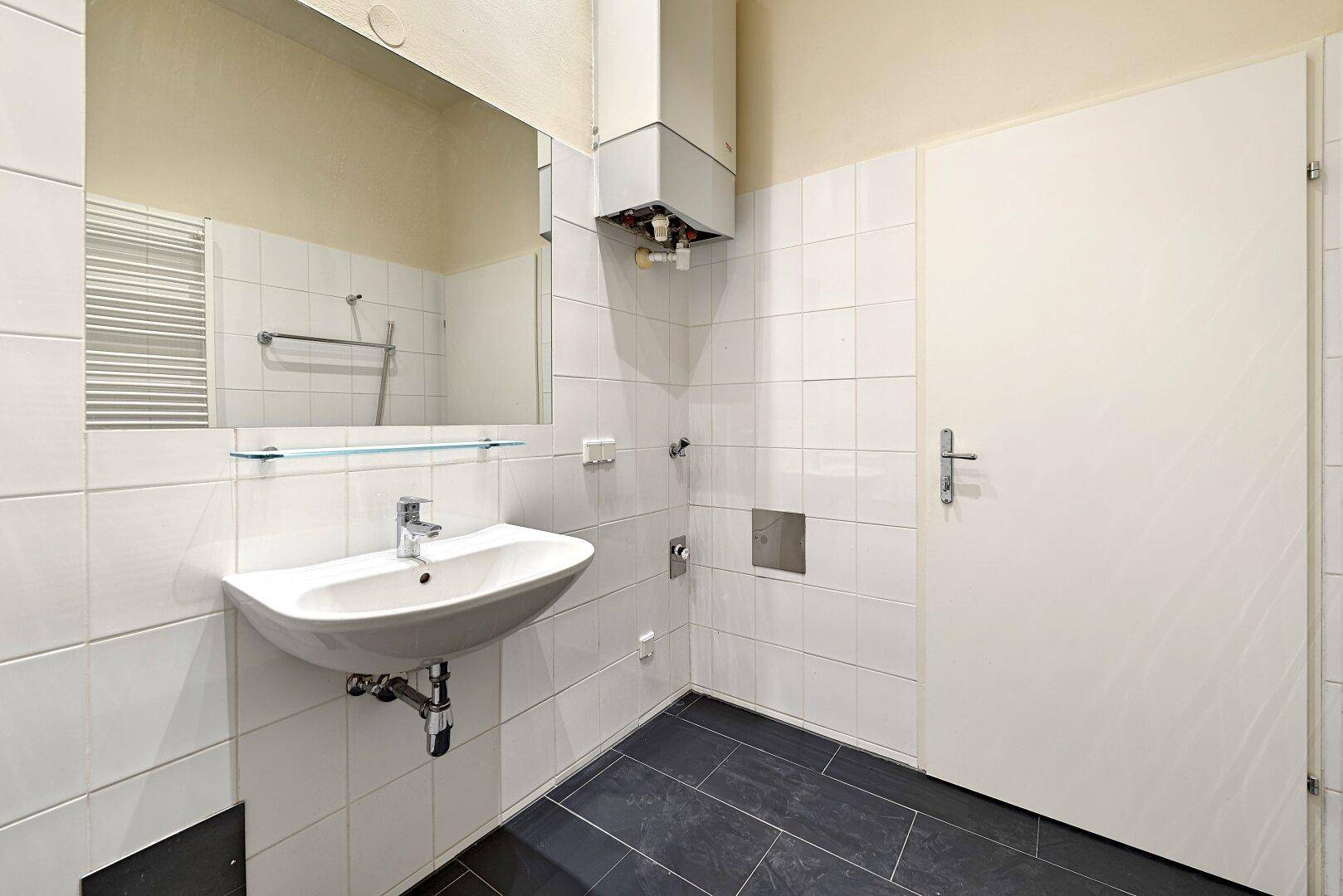 Helles Badezimmer mit Waschbecken, großem Spiegel und weißen Wandfliesen, funktional gestaltet.