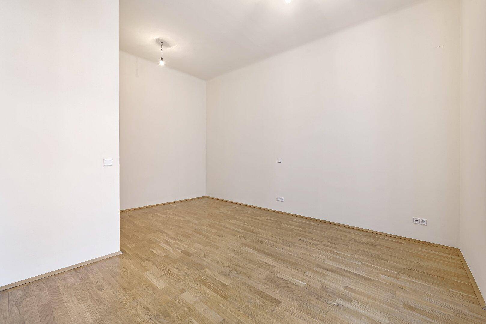 Schlichtes Zimmer mit Parkettboden und weißen Wänden, bietet eine neutrale Basis für Einrichtung.