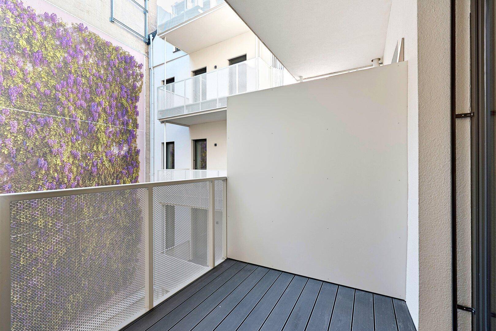 Moderner Balkon mit Holzboden und Blick auf die begrünte Fassade des Nachbargebäudes.