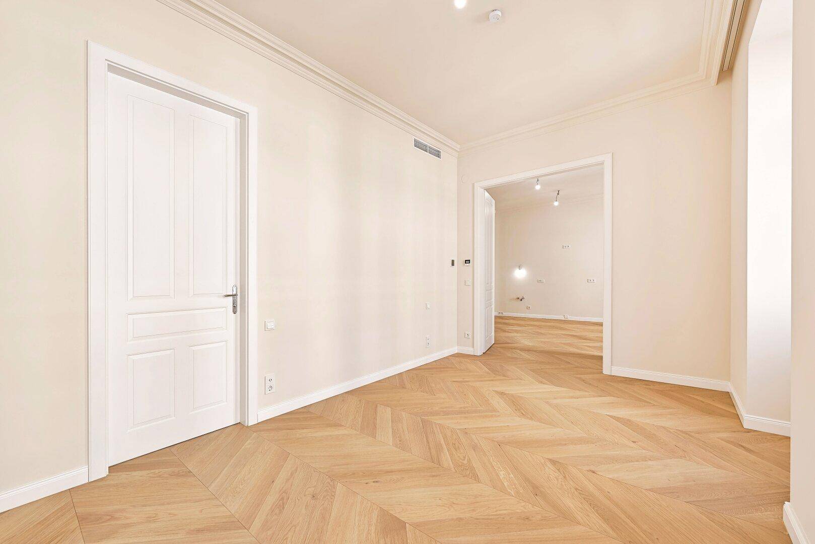 Geräumiges Zimmer mit Fischgrätparkett und weißer Tür, bereit für individuelle Gestaltung.