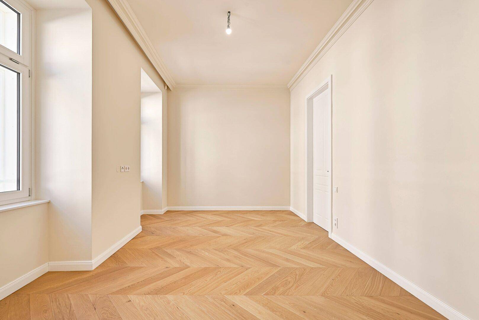 Leeres Zimmer mit Fischgrätparkett und großem Fenster, ideal als Schlaf- oder Arbeitszimmer.