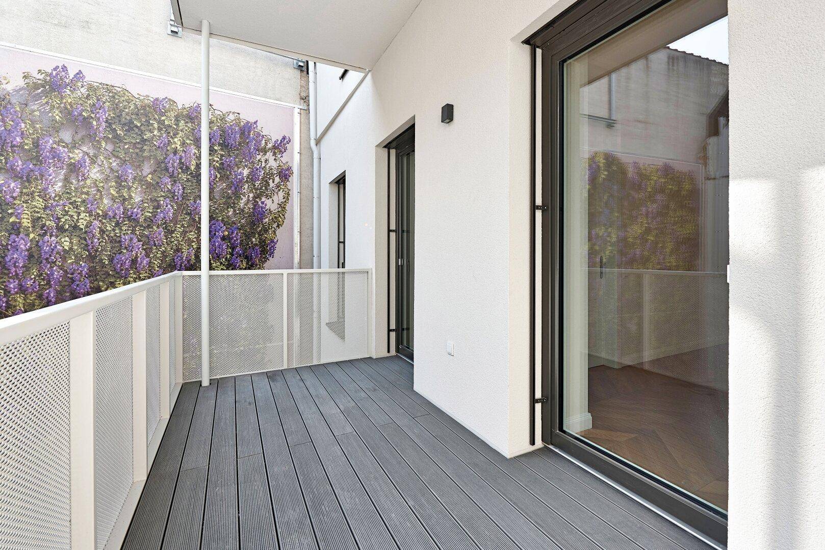 Heller Balkon mit modernem Bodenbelag und einer dekorativen Wandbegrünung, ideal zum Entspannen.